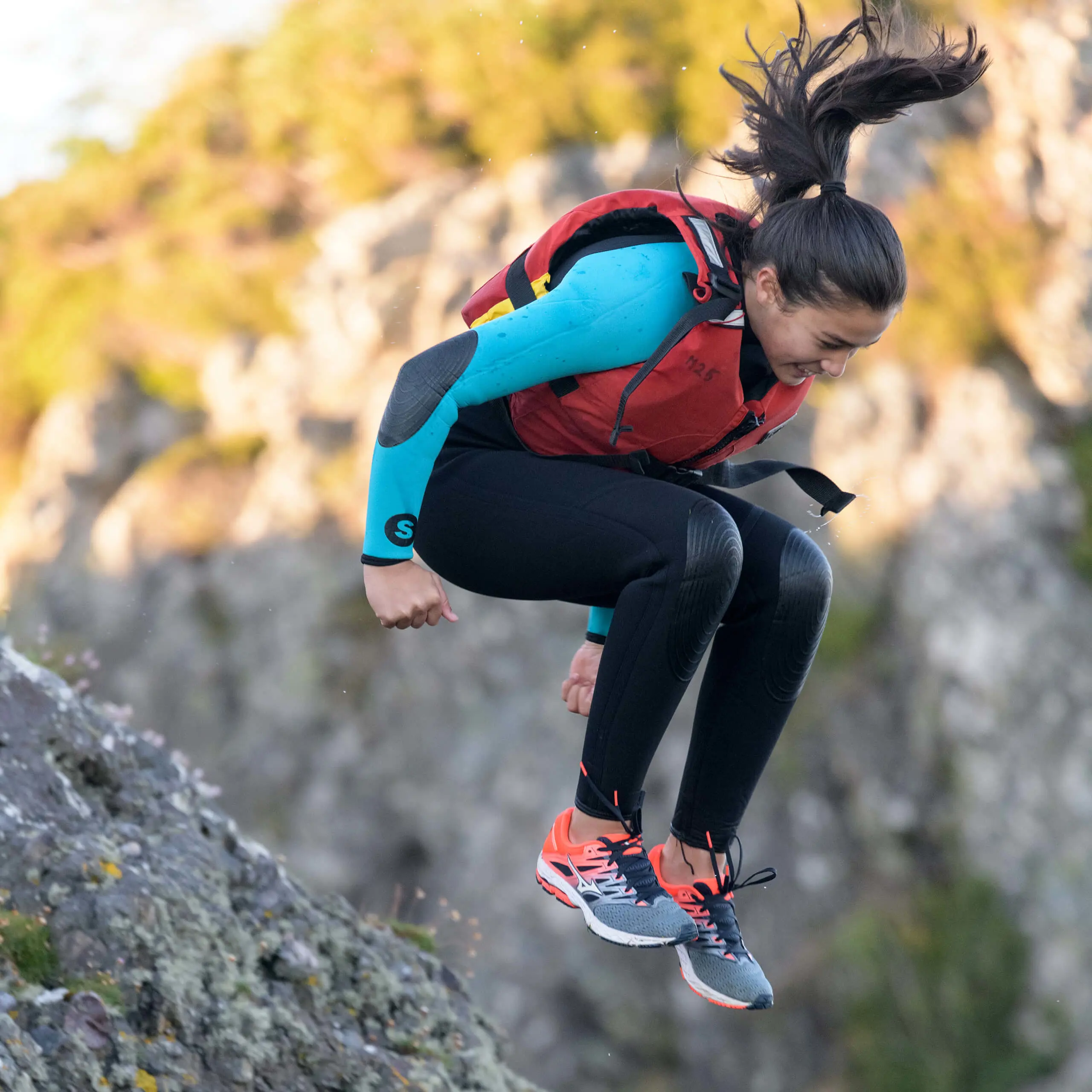 Smiling Gordonstoun student jumps from the cliffs into the water wearing a life jacket.