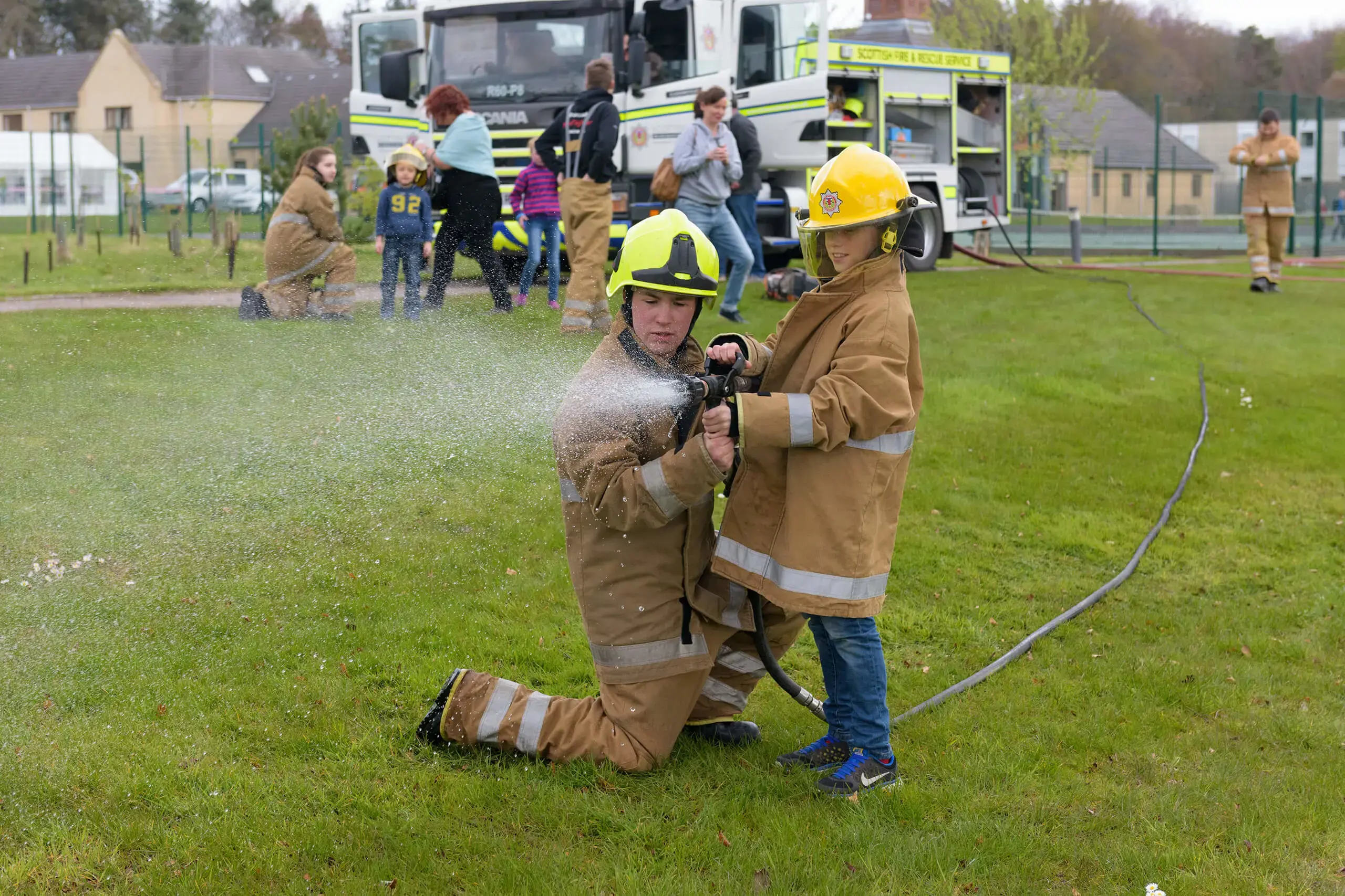 Student fire service member at community event helping young child hold the fire hose for a demonstration