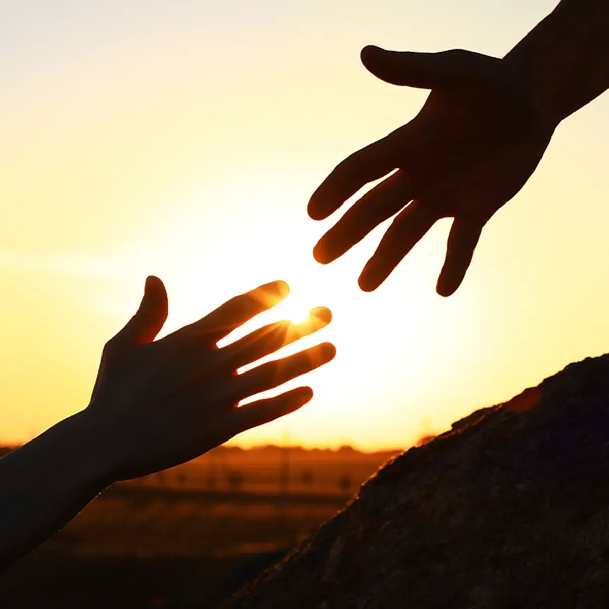 Two Hands Reaching Put to Each Other In Front of a Sunset