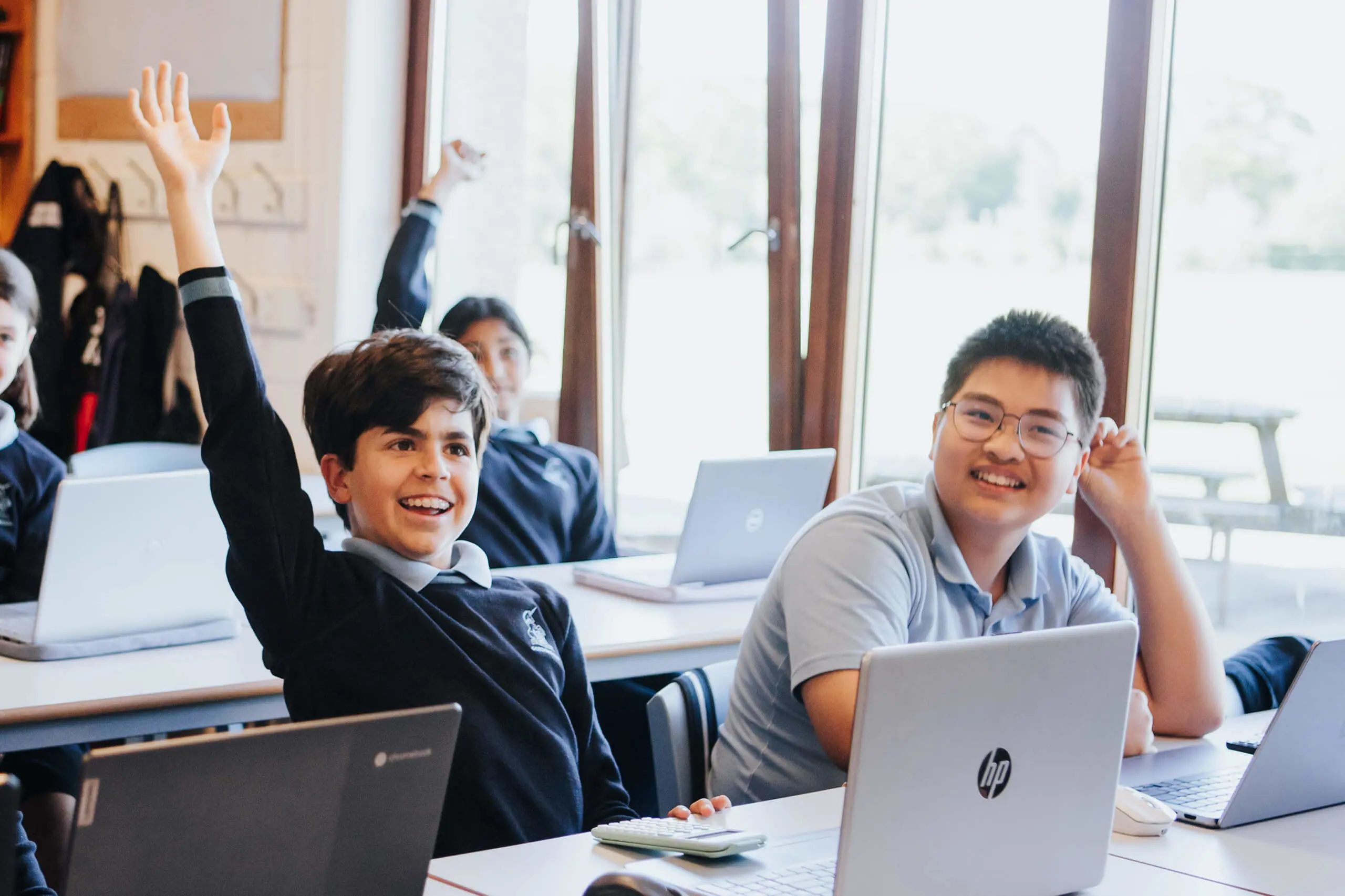 Prep pupils in class with hands up to answer a question, smiling