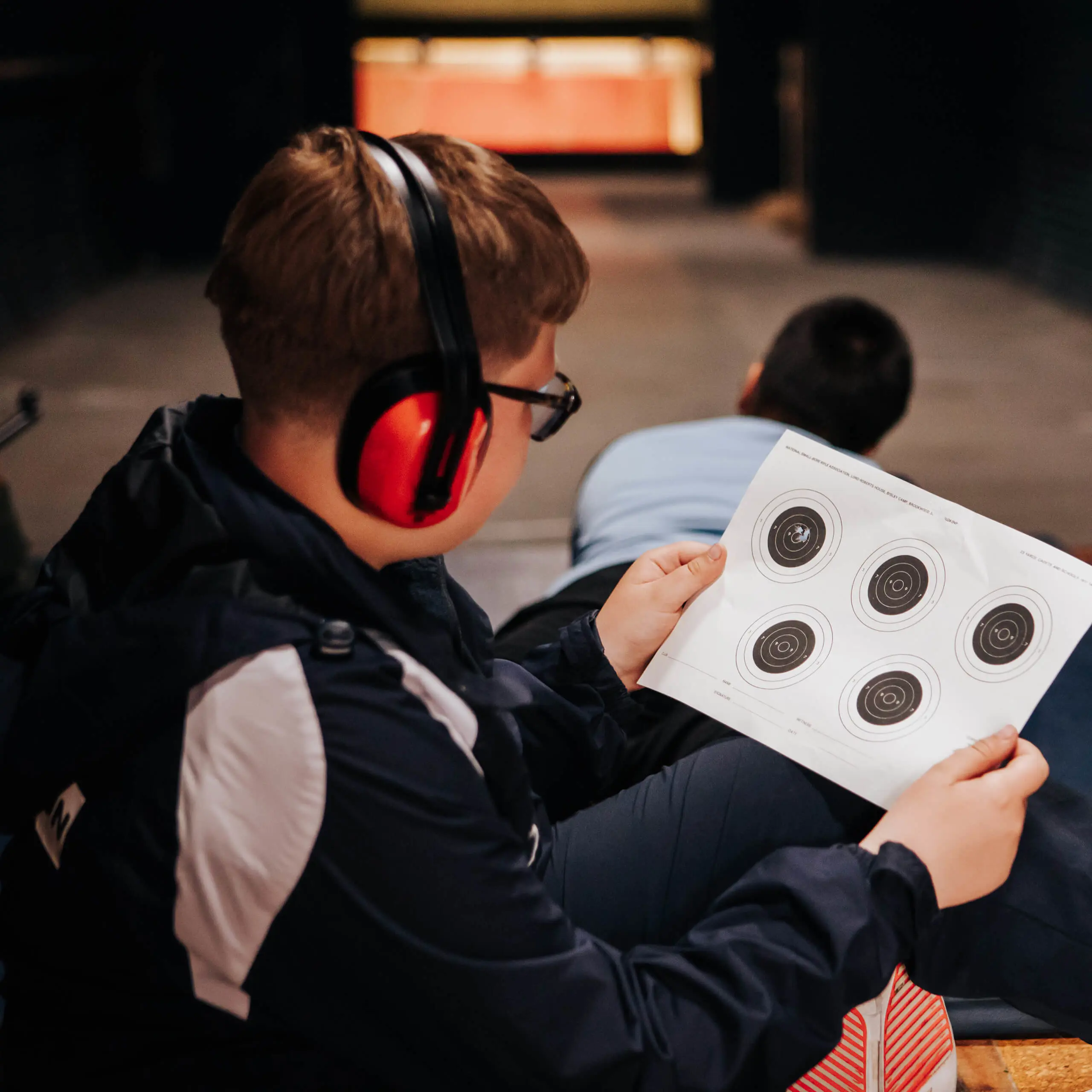 Gordonstoun Prep pupil at a shooting range wearing ear defenders and inspecting used targets.