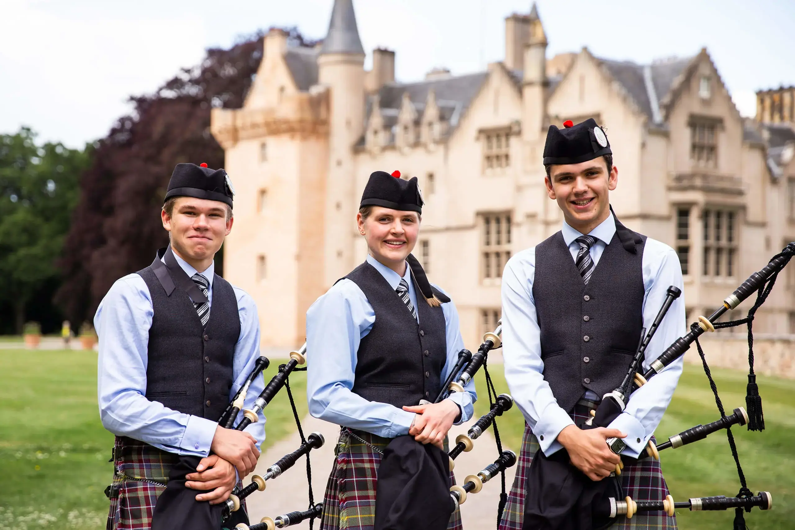 Three of Gordonstoun’s award winning pipe band members stand outside the front of Brodie castle before a performance.