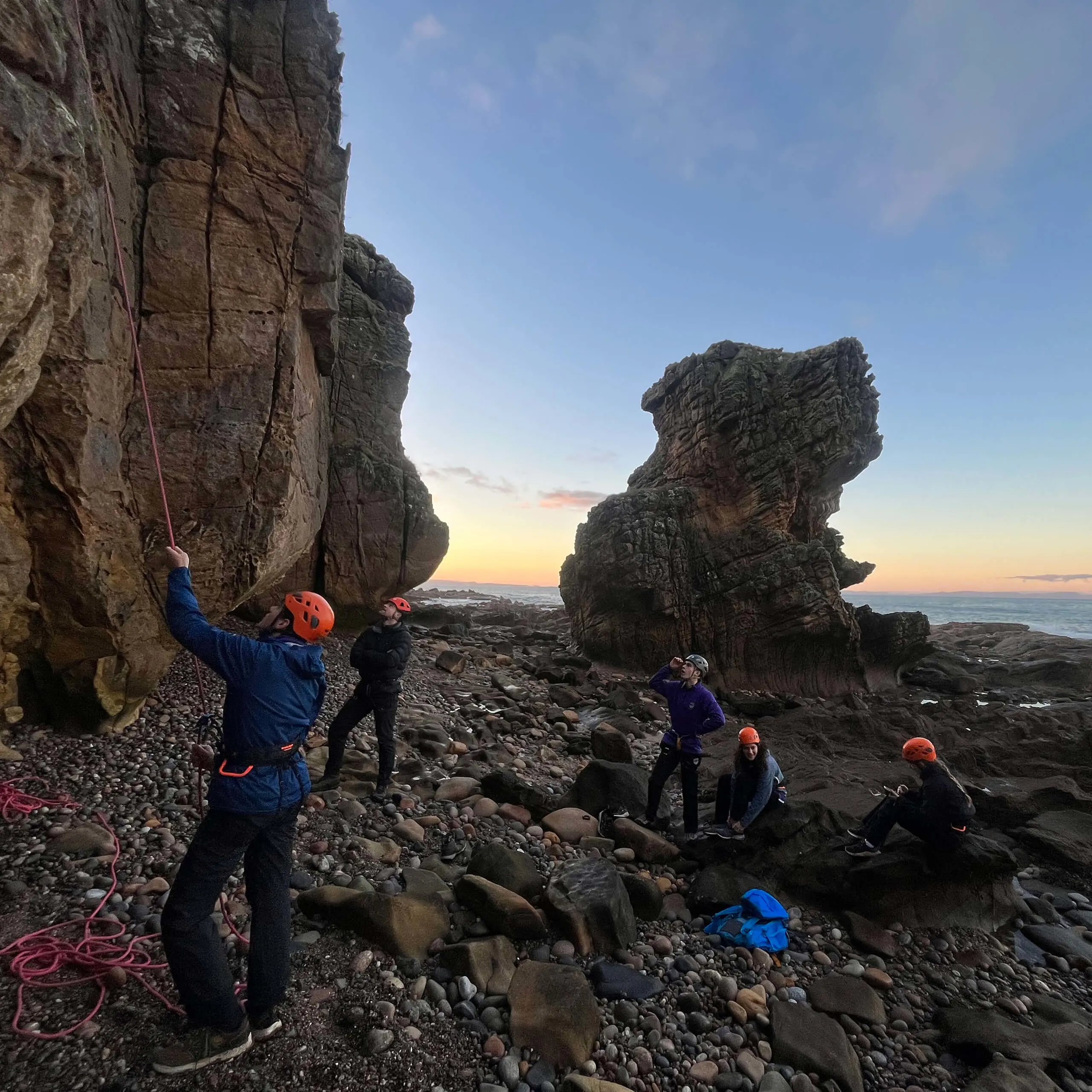 Gordonstoun pupils and teachers on beach by cliffs, wearing helmets