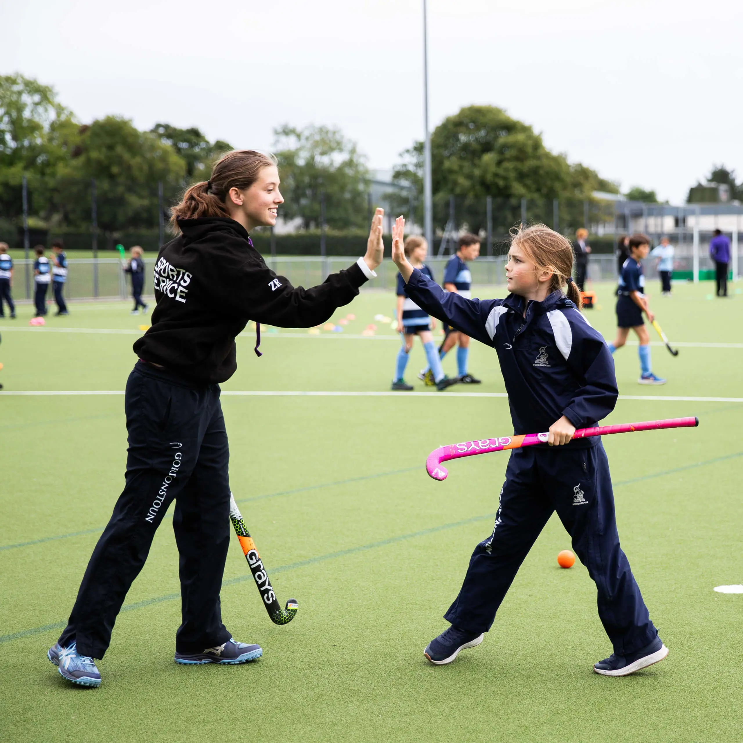 Student member of Gordonstoun's Sports Service help to coach primary age pupils to play hockey.