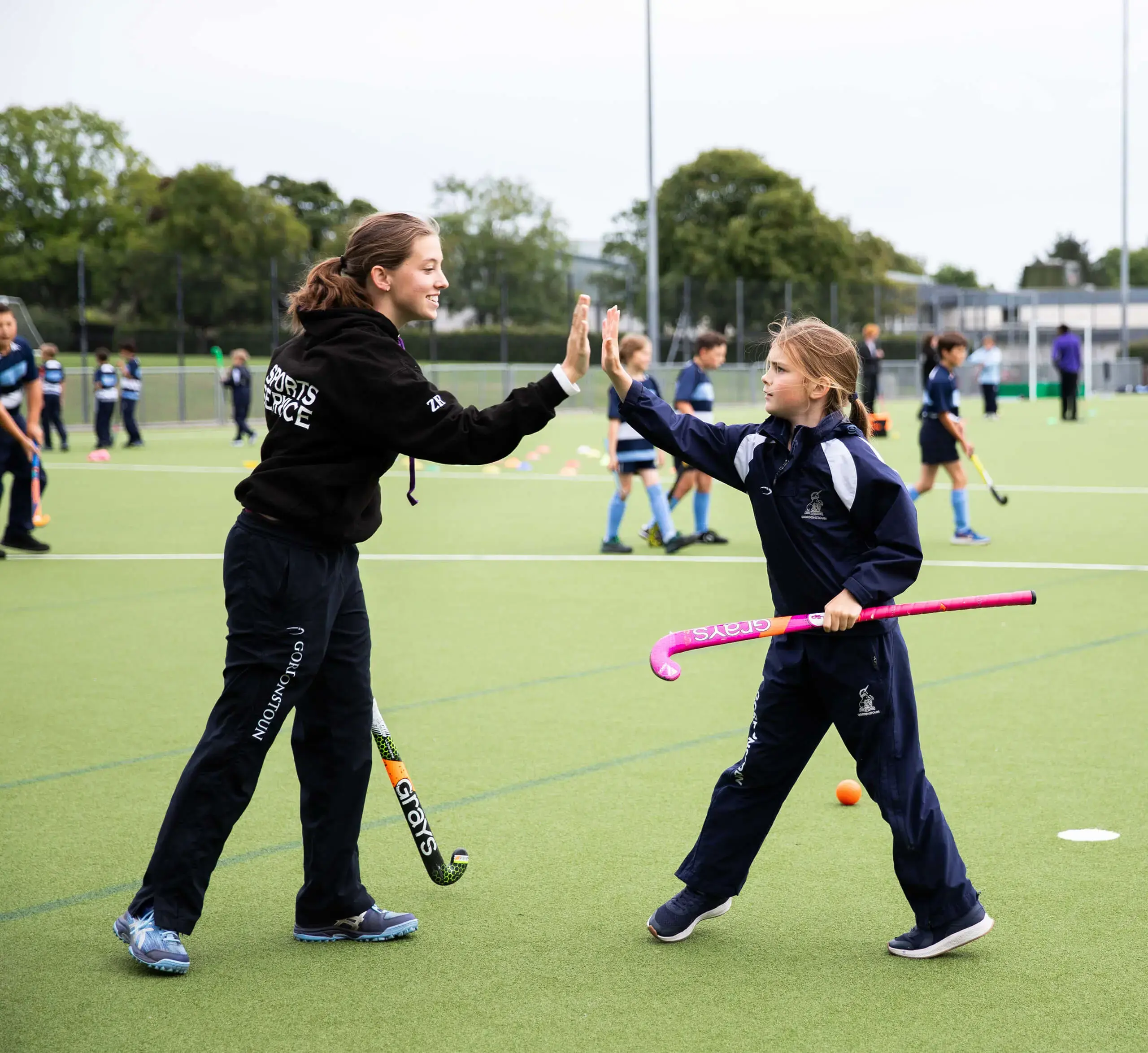 Senior School student high fives a prep school student during a sports service hockey training session.